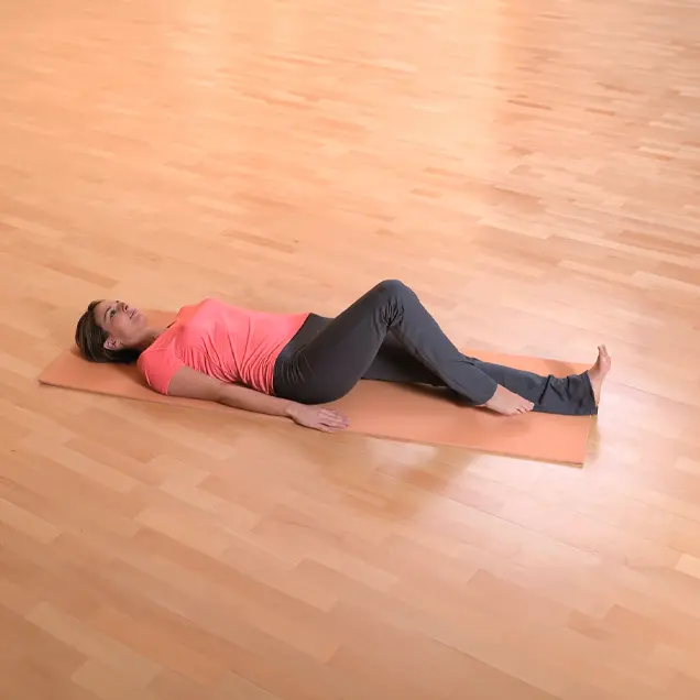 Frau liegt auf einer Yogamatte und winkelt ein Bein leicht an.