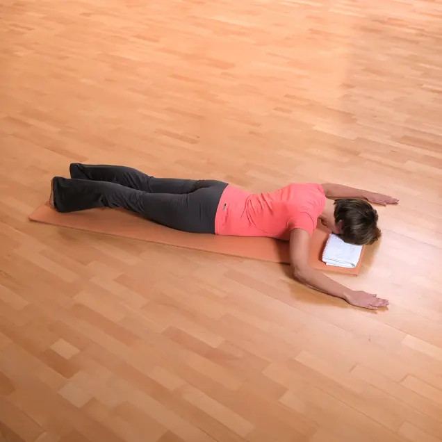 Frau liegt auf dem Bauch auf einer Yogamatte und schaut nach unten.