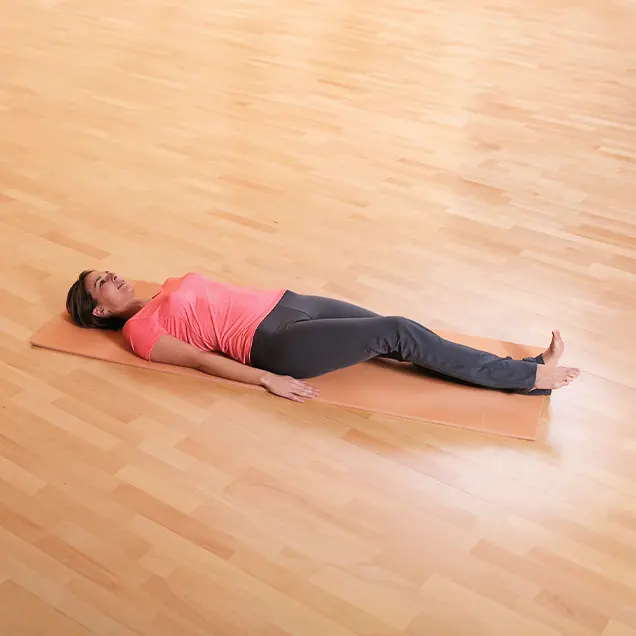 Frau liegt auf dem Rücken auf einer Yogamatte und hebt ein Bein leicht an.